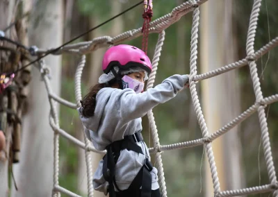Niña con casco rosado cruzando una red de cuerdas en el canopy