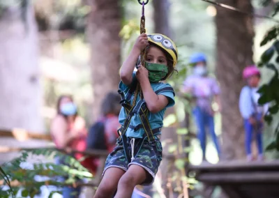 Niño con casco colgando de una tirolesa entre los árboles