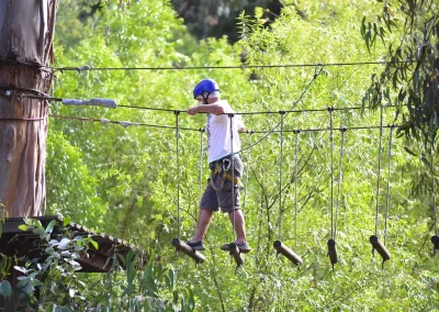 Niño con casco cruzando un puente colgante de madera entre los árboles
