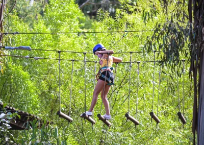 Niña con casco cruzando un puente colgante de madera en altura