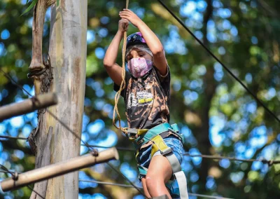 Niño con arnés escalando una cuerda junto a un tronco en el canopy